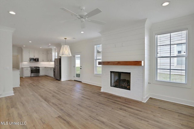 unfurnished living room featuring light hardwood / wood-style floors, a large fireplace, plenty of natural light, and ceiling fan