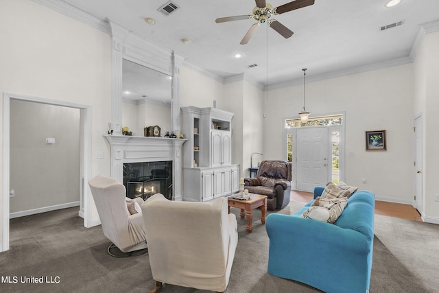 carpeted living room featuring a towering ceiling, ornamental molding, a tile fireplace, and ceiling fan