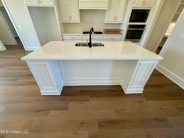 kitchen with oven, white cabinetry, backsplash, and an island with sink