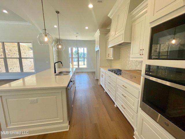 kitchen with sink, appliances with stainless steel finishes, decorative light fixtures, and an island with sink