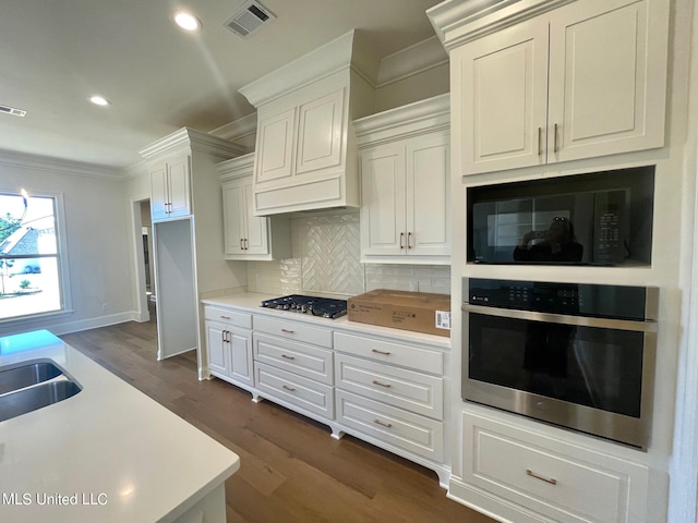 kitchen featuring decorative backsplash, dark wood-type flooring, ornamental molding, white cabinetry, and appliances with stainless steel finishes