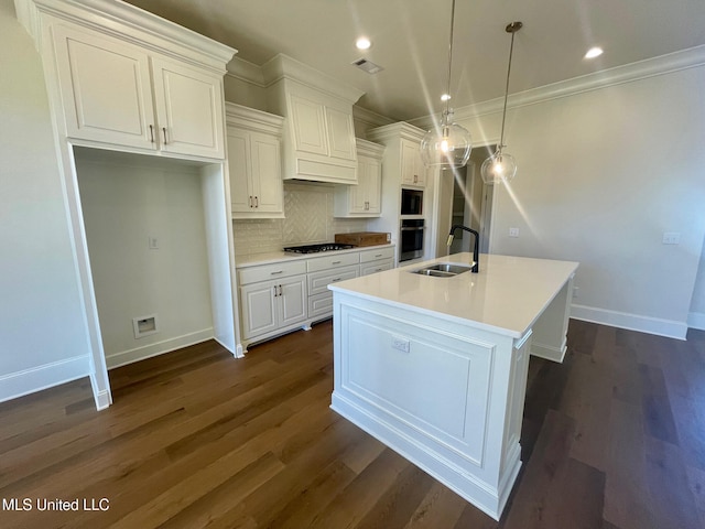 kitchen with appliances with stainless steel finishes, dark hardwood / wood-style flooring, decorative light fixtures, white cabinets, and a center island with sink