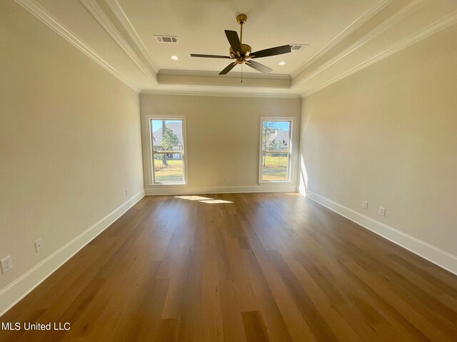 empty room with ornamental molding, ceiling fan, a tray ceiling, and dark hardwood / wood-style flooring