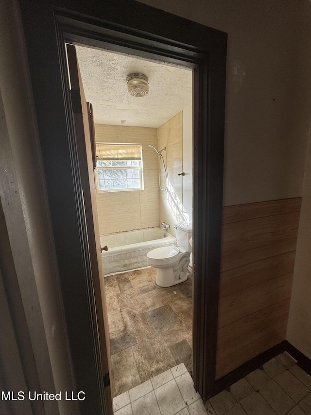 bathroom with tiled shower / bath combo, toilet, and a textured ceiling