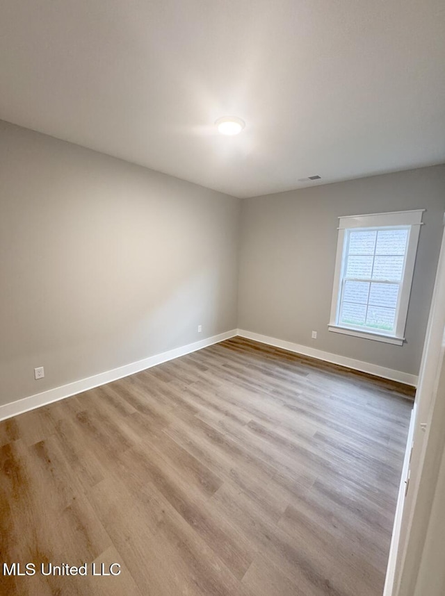 spare room featuring wood finished floors, visible vents, and baseboards