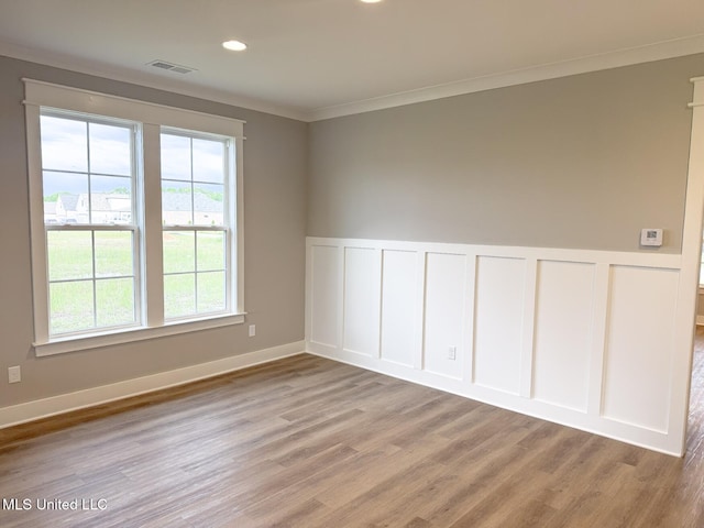 empty room featuring light wood finished floors, a decorative wall, a wainscoted wall, and visible vents