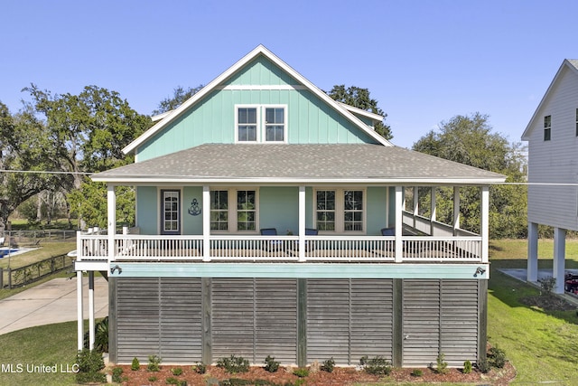 view of front of property with board and batten siding, a front yard, covered porch, and roof with shingles