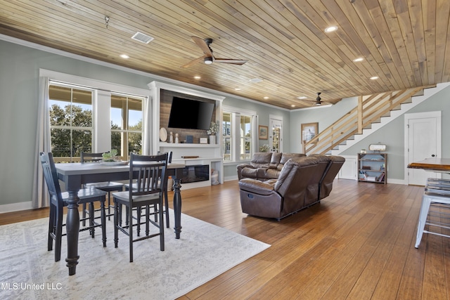 living room with hardwood / wood-style flooring, a large fireplace, crown molding, wood ceiling, and stairs