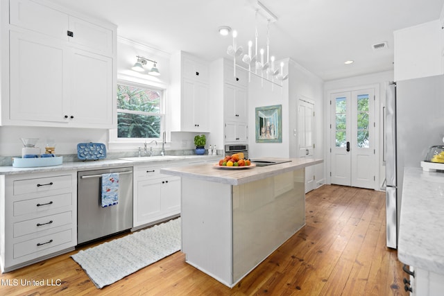 kitchen featuring stainless steel appliances, a sink, a kitchen island, white cabinetry, and pendant lighting