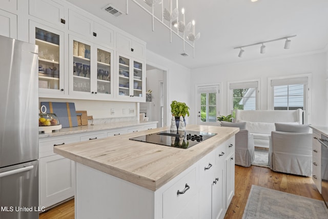 kitchen featuring glass insert cabinets, a kitchen island, white cabinetry, freestanding refrigerator, and decorative light fixtures