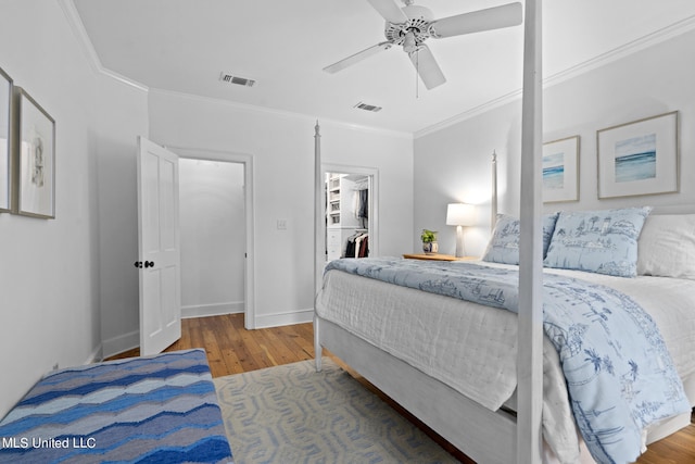 bedroom with ornamental molding, visible vents, a spacious closet, and wood finished floors