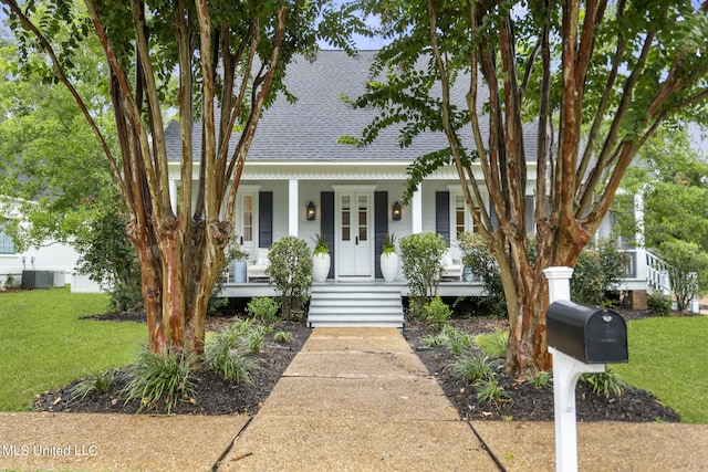 view of front of property with covered porch, a front yard, central AC unit, and roof with shingles