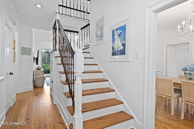 stairway with recessed lighting, an inviting chandelier, ornamental molding, wood finished floors, and baseboards