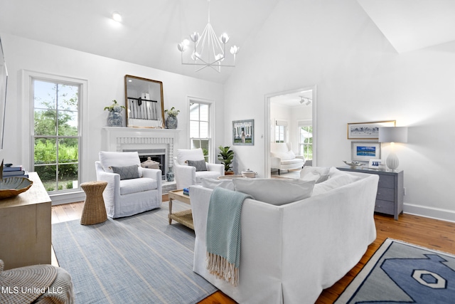 living area featuring baseboards, light wood-style floors, an inviting chandelier, a brick fireplace, and high vaulted ceiling