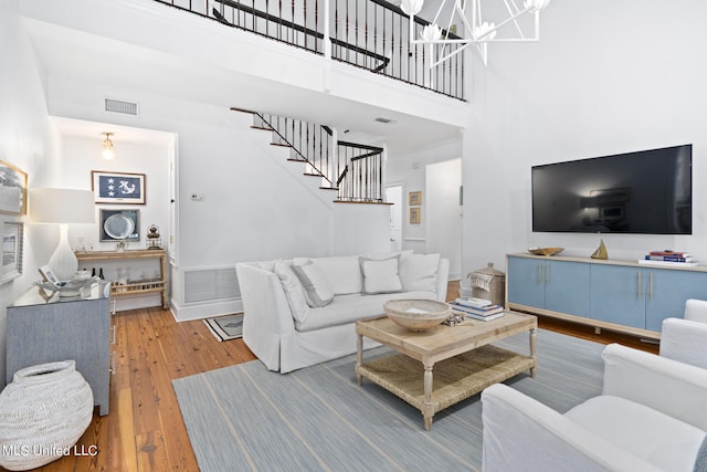 living area featuring a notable chandelier, wood finished floors, a towering ceiling, visible vents, and stairway