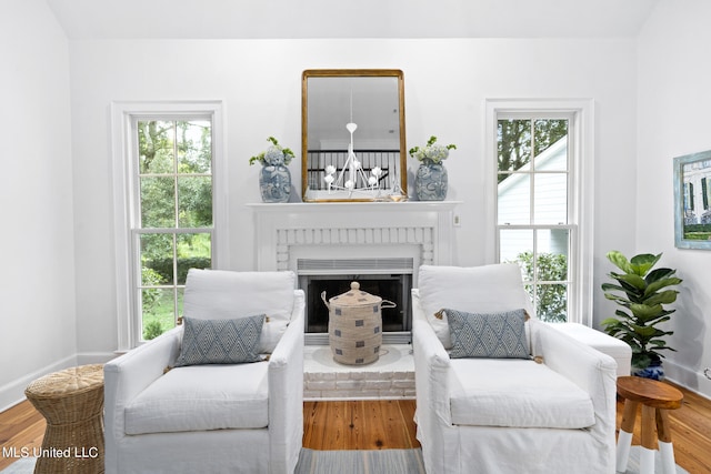 sitting room with a brick fireplace, wood finished floors, and baseboards