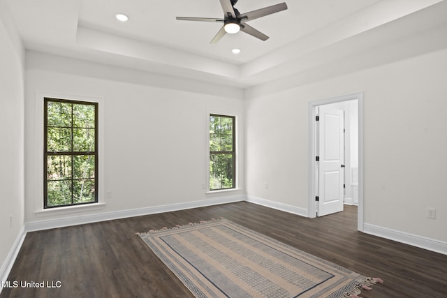 unfurnished room featuring baseboards, a tray ceiling, and dark wood-style floors