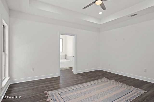 unfurnished bedroom featuring visible vents, a raised ceiling, dark wood-type flooring, and baseboards