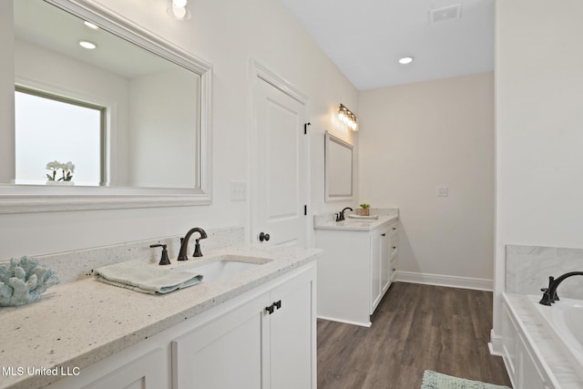 full bathroom featuring visible vents, wood finished floors, a bath, two vanities, and a sink