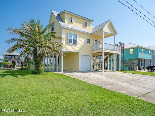 raised beach house with stairs, a front yard, metal roof, a garage, and driveway