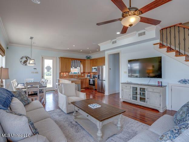 living room featuring wood finished floors, visible vents, recessed lighting, ornamental molding, and stairs