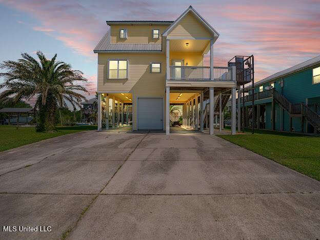 coastal home with driveway, a front lawn, stairway, metal roof, and a carport