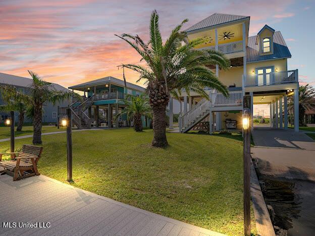 coastal home featuring a lawn, driveway, metal roof, and stairs