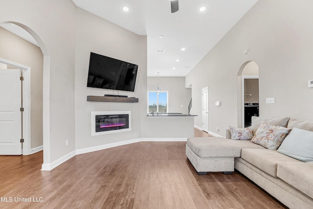 living area featuring arched walkways, a glass covered fireplace, wood finished floors, and baseboards