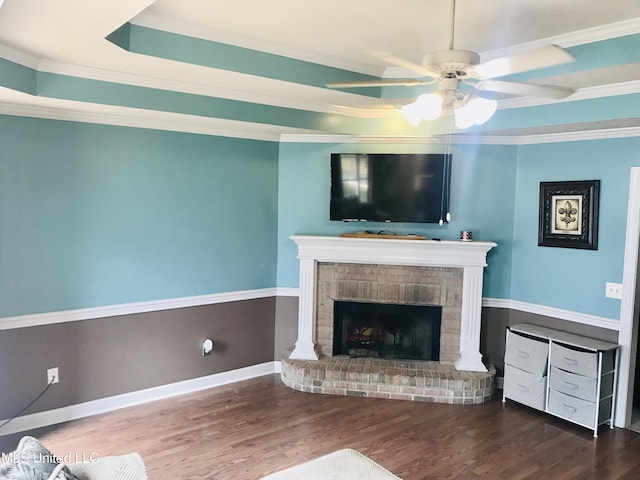 unfurnished living room with a tray ceiling, a brick fireplace, wood finished floors, and ornamental molding