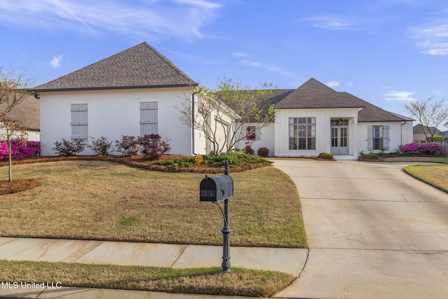 view of front of home featuring roof with shingles, driveway, brick siding, and a front yard