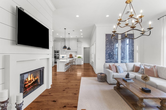 living room with crown molding, a glass covered fireplace, recessed lighting, and wood finished floors