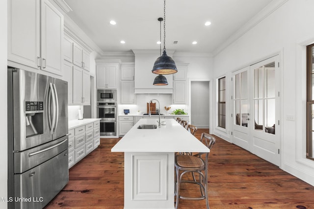 kitchen with ornamental molding, appliances with stainless steel finishes, a center island with sink, and light countertops
