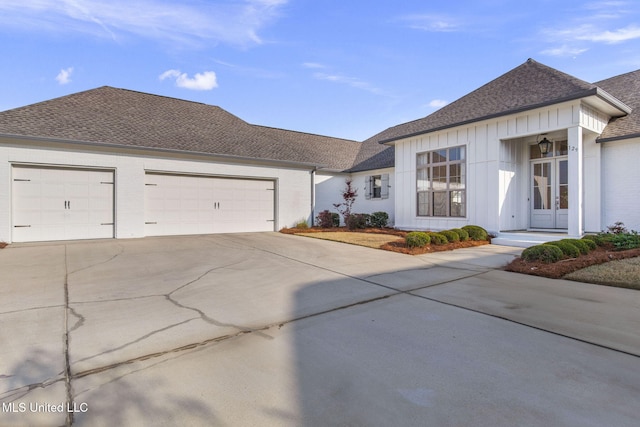 single story home with a shingled roof, an attached garage, board and batten siding, french doors, and driveway