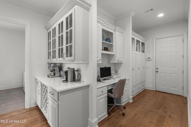 home office with ornamental molding, dark wood-type flooring, built in desk, and visible vents