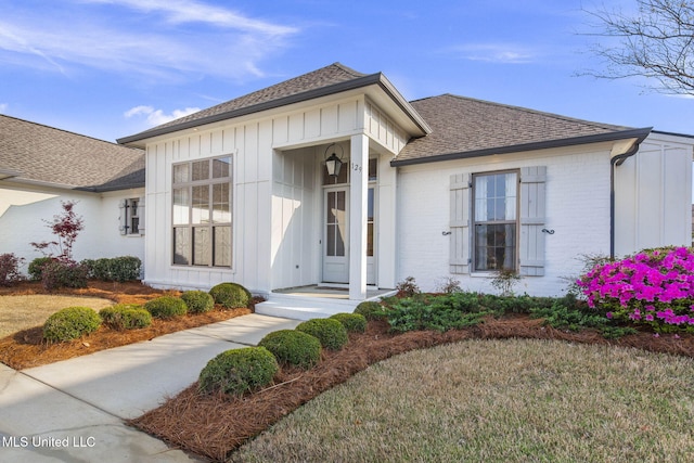 view of front of house featuring brick siding, a shingled roof, and board and batten siding