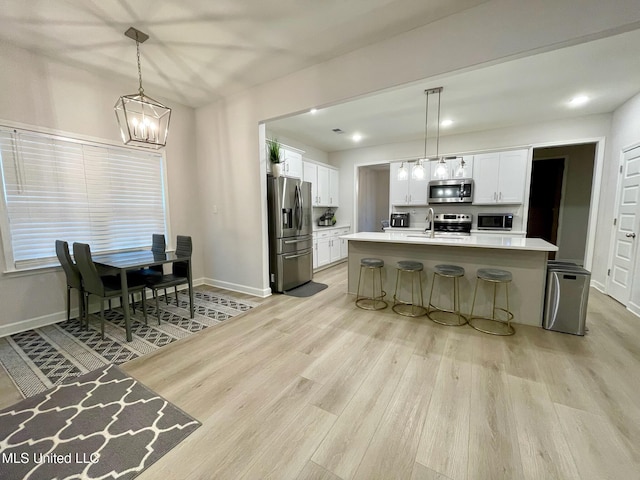 kitchen with decorative light fixtures, a center island with sink, light wood-type flooring, appliances with stainless steel finishes, and white cabinets