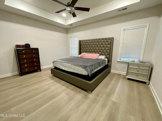 bedroom featuring ceiling fan, light hardwood / wood-style floors, and a tray ceiling