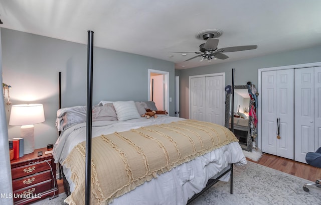 bedroom featuring hardwood / wood-style floors, multiple closets, and ceiling fan