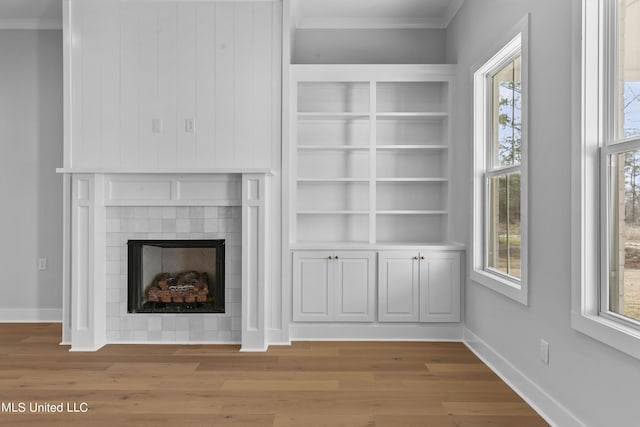 unfurnished living room featuring crown molding, plenty of natural light, a fireplace, and light wood-style flooring