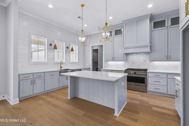 kitchen with glass insert cabinets, a center island, high end stainless steel range, light countertops, and a sink