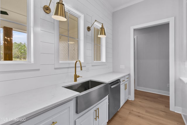 kitchen featuring white cabinets, light stone countertops, stainless steel dishwasher, light wood-style floors, and a sink