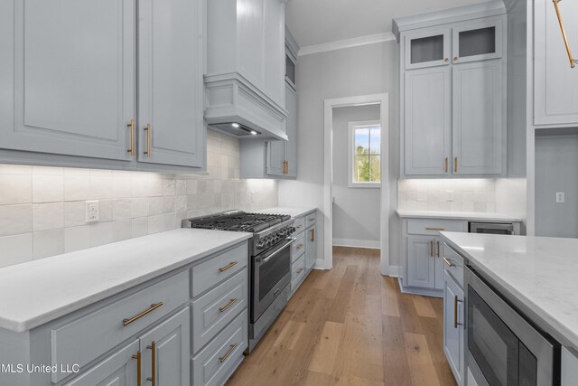 kitchen with stainless steel stove, glass insert cabinets, ornamental molding, light stone countertops, and light wood-type flooring