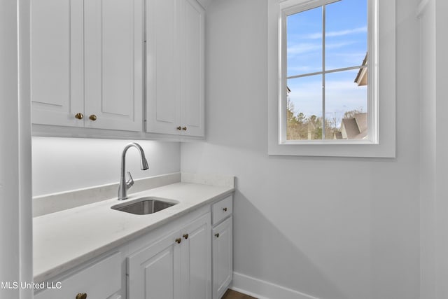 interior space with baseboards, a sink, white cabinetry, and light stone countertops