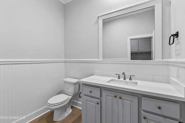 half bathroom featuring toilet, vanity, wood finished floors, and wainscoting