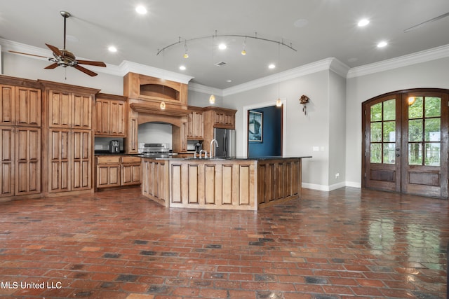 kitchen featuring brick floor, a kitchen island with sink, baseboards, dark countertops, and crown molding