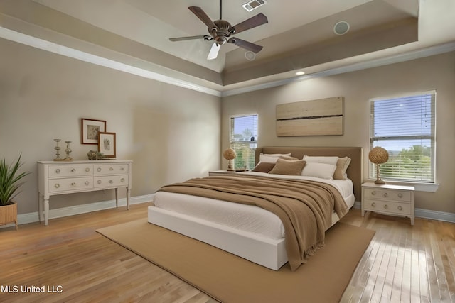 bedroom with a tray ceiling, multiple windows, and light wood-style floors