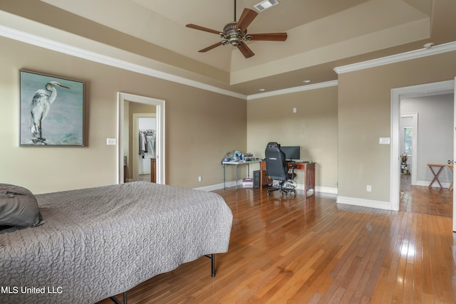 bedroom featuring a tray ceiling, crown molding, wood-type flooring, visible vents, and baseboards