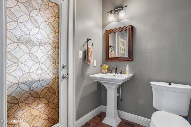 half bathroom with brick floor, toilet, and baseboards