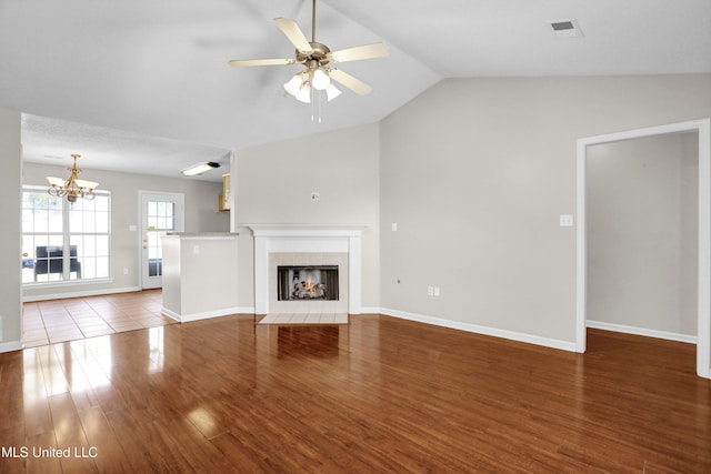 unfurnished living room featuring lofted ceiling, dark hardwood / wood-style floors, ceiling fan with notable chandelier, and a tile fireplace