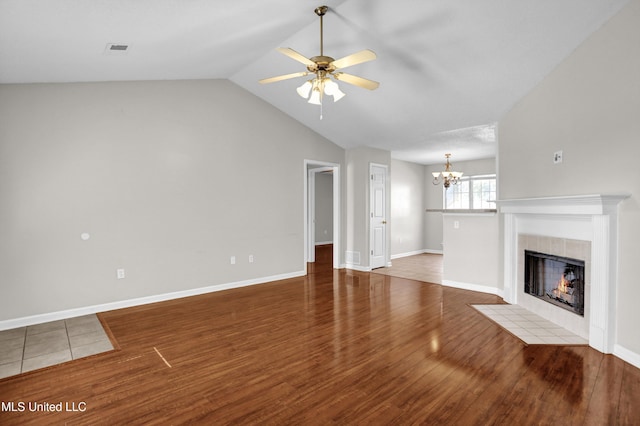 unfurnished living room featuring a tiled fireplace, hardwood / wood-style flooring, ceiling fan with notable chandelier, and vaulted ceiling